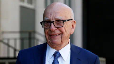 Reuters Headshot of Rupert Murdoch standing outside a building wearing a suit and tie and smiling