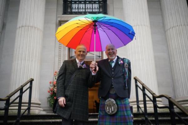 Andy Lambert and Mel Fawcus smile under a rainbow coloured umbrella on the steps of the town hall