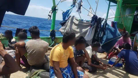 Handout The Tamil migrants, with their faces blurred or turned away from the camera, sitting on the deck of a boat, with washing on lines around them, as they sailed through the Indian Ocean