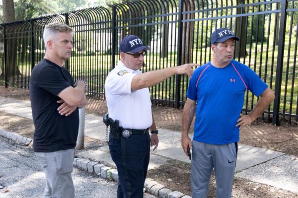 A Lieutenant with NYPD Community Affairs talks to Scott Herkert, left, and John Tabacco. Herkert lives next to the academy had has a speaker playing tell the migrants to leave.