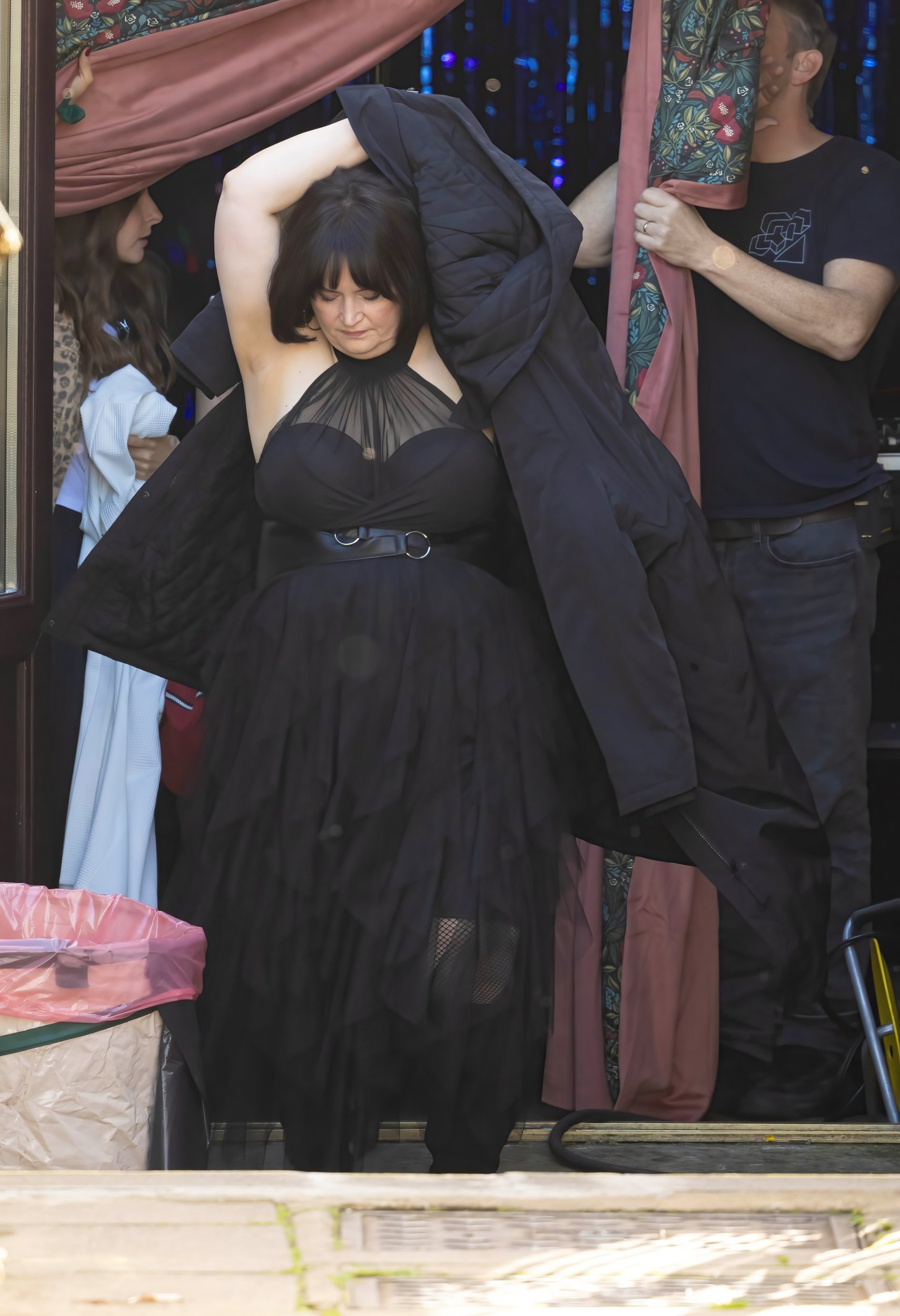 Ruth Jones as Nessa, wearing a black dress and putting on a black coat on the Gavin and Stacey set