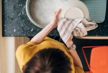 Man crouching down to put washing into his washing machine in his kitchen. He is in the Northeast of England.