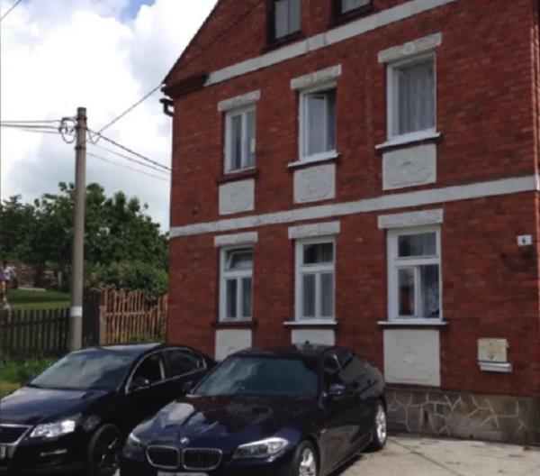 A three-story house with two black cars parked outside.