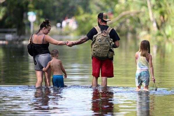 Dustin Holmes and his girlfriend, Hailey Morgan, holding hands with her children, Aria Skye Hall and Kyle Ross, while returning to their flooded home following Hurricane Helene in Crystal River, Fla.