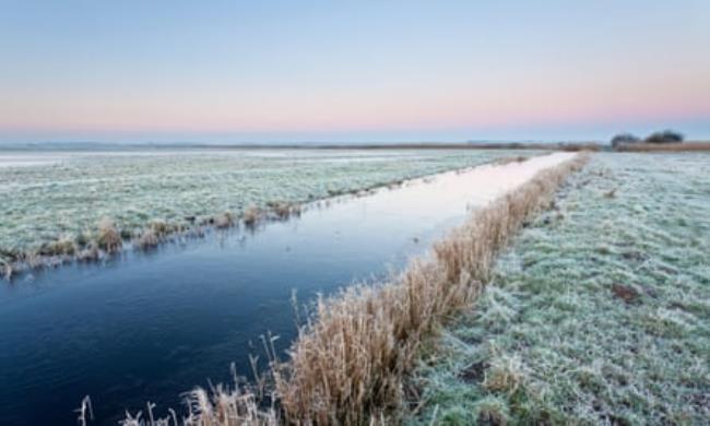 A river that is part of the Halvergate Marshes with frost on the grass