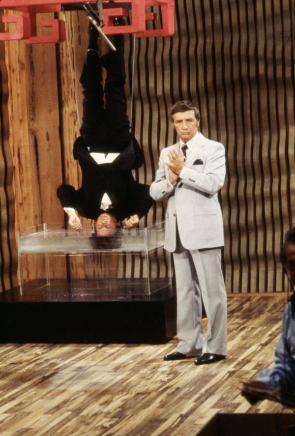 Bob Yerkes and Richard Dawson in a sketch for the 'Bizarre' TV series, with one man upside down on stage, 1979
