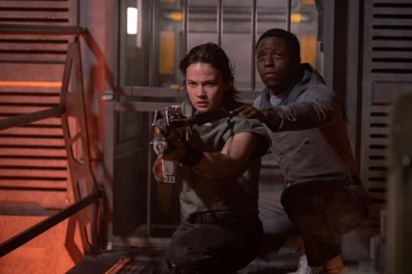 Cailee Spaeny as Rain holds a gun up and David Jonsson as Andy holds her shoulder from behind in a scene from Alien: Romulus