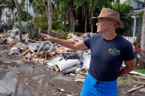 Man in hat gestures toward street piled with debris.