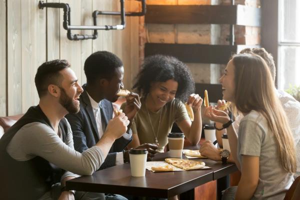 A group of young adults talking and laughing over coffee and pizza.