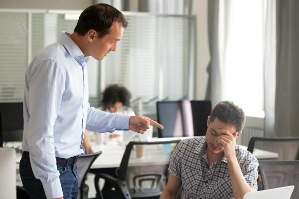 A man points his finger while speaking down to another man, who is seated an has his head resting against his hand