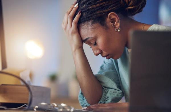 A young woman rests her head against her hand with an exhausted look on her face