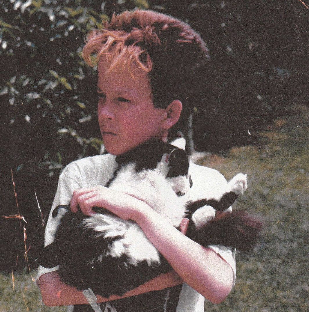 Chas as a young teen, holding a cat in his arms while standing in his garden