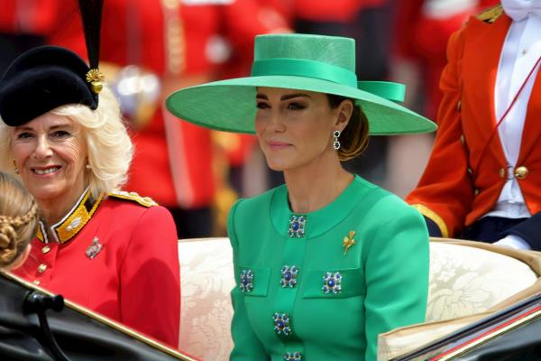 Princess Catherine sits next to Queen Camilla and wears a green hat and suit.