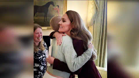 Kensington Palace  The Princess of Wales hugging Liz Hatton - the princess is wearing a dark red outfit with the side of her head visible. Liz is wearing a green jumper and her head is shaved. 