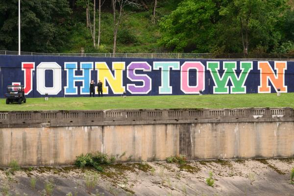 Two men standing in front of a huge painted sign that says 'Johnstown.'
