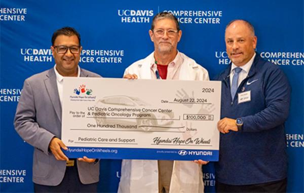 Three men hold oversized check for $100,000 made out to UC Davis Comprehensive Cancer Center & Pediatric oncology Program for 