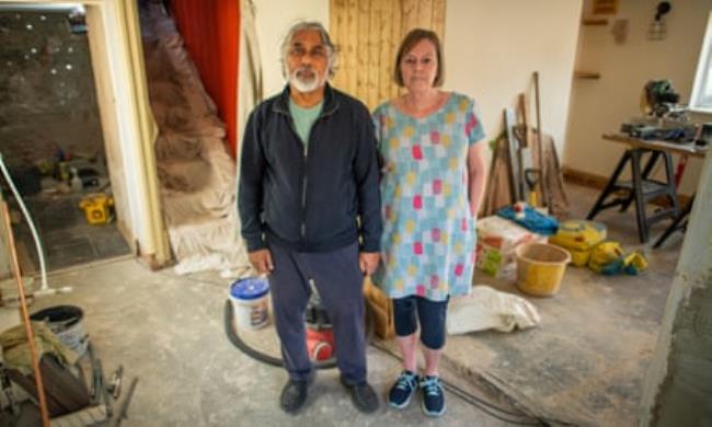 A man and woman stand on a bare floor in their house