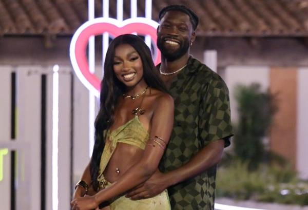 Mimii Ngulube and Josh Oyinsan on the Love Island final. He is stood behind her, holding onto her waist. They are both smiling. Mimi is wearing a light green dress with cut-out on the stomach and Josh is wearing a dark green shirt