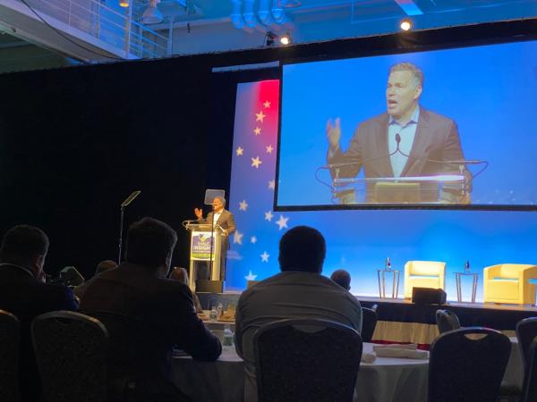 Dave McCormick speaks at conference with attendees watching him on stage and on screen.