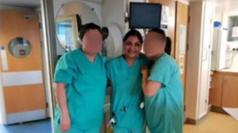 Tanya Nasir/Facebook Tanya Nasir穿着护士制服在医院病房里,双臂环绕着另外两名护士(面部模糊)