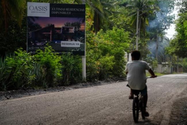 A child riding a bicycle next to a sign advertising a housing development