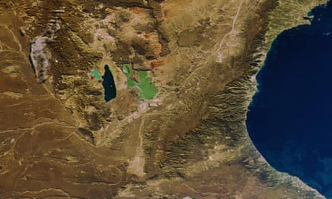 An aerial picture showing brown arid looking land with a navy blue lake to the left and a much lighter turquoise green lake to the right.