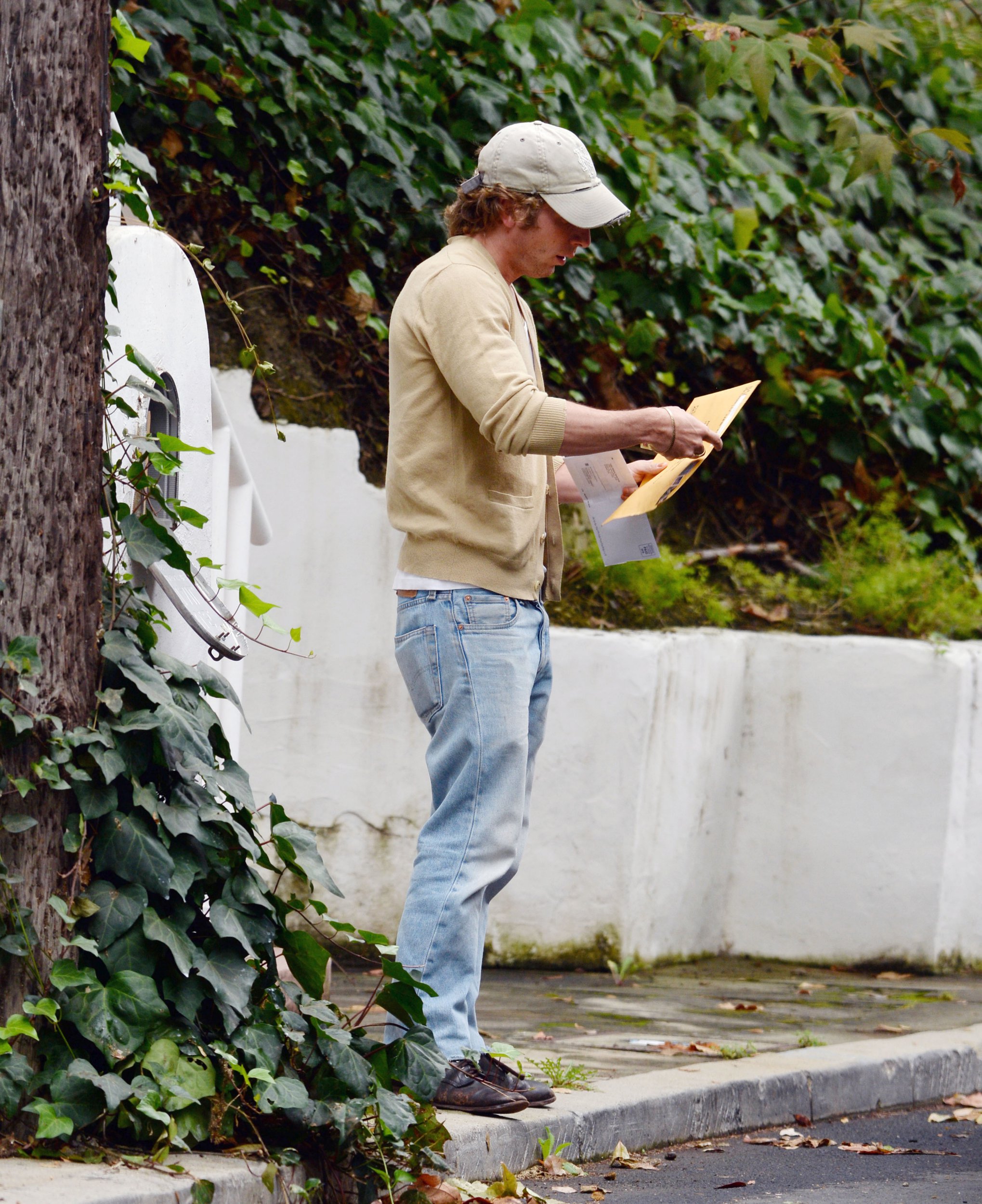 Jeremy Allen White holds an envelope by a car on the street