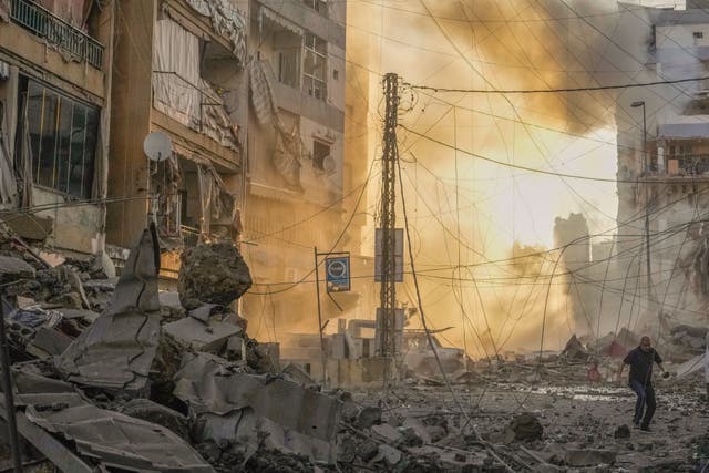 A man runs for cover as smoke rises in the background following an Israeli air strike in Dahiyeh, Beirut, Lebanon