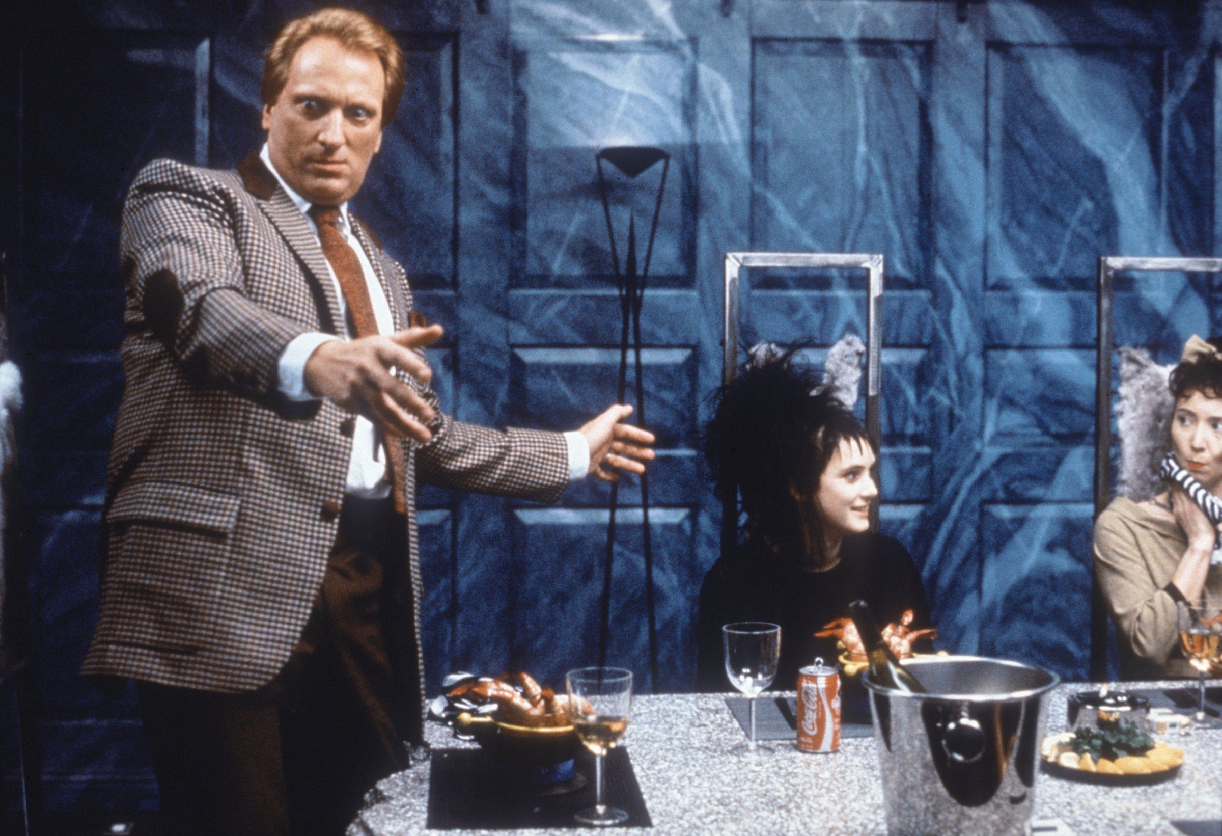 Jeffrey Jones as Charles Deetz stands at the dinner table next to Winona Ryder seated as Lydia Deetz in a scene from Beetlejuice