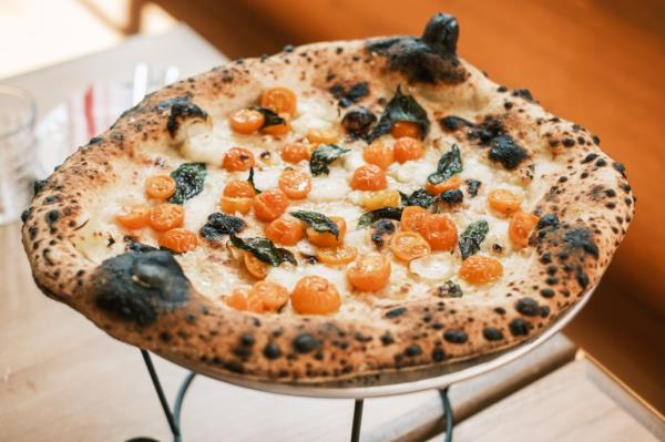 Pizza, topped with small tomatoes, sitting on a stand atop a table