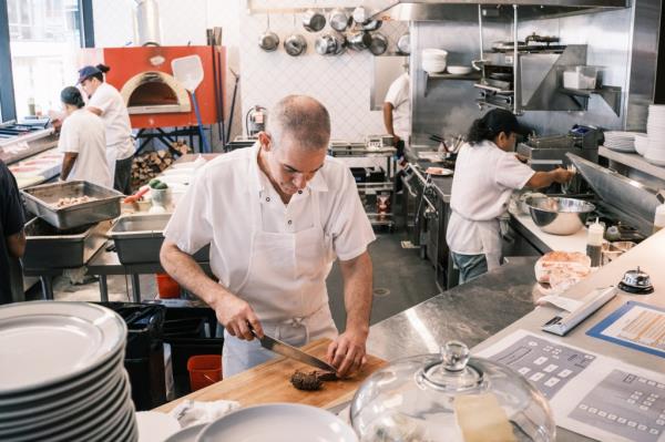 Chef de cuisine Daniel Rubenfeld cutting food in the kitchen of Roberta's Midtown, Manhattan
