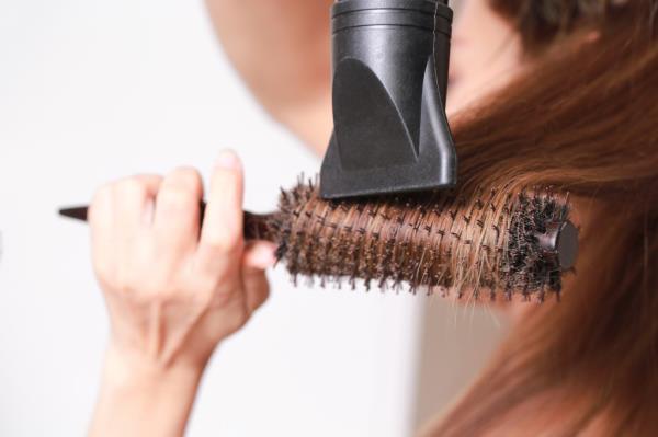 A woman styles her hair with a brush and blow dryer.