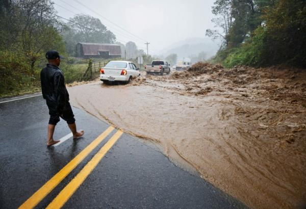 A local resident watches cars traverse a treacherous stretch of flooded road.