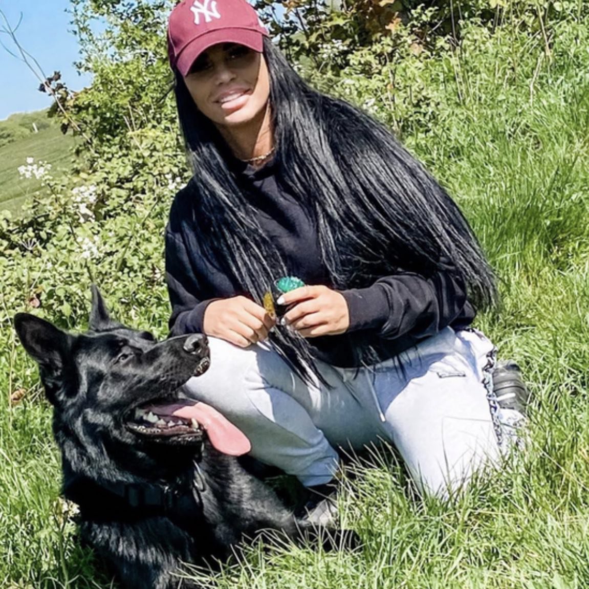 Katie Price in a field kneeling next to a black dog