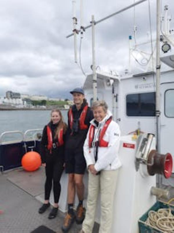 Three people wearing lifejackets on a boat at sea (woman, man, woman)