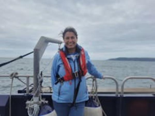 Woman in blue jacket and red lifejacket standing on boat at sea, grey sky