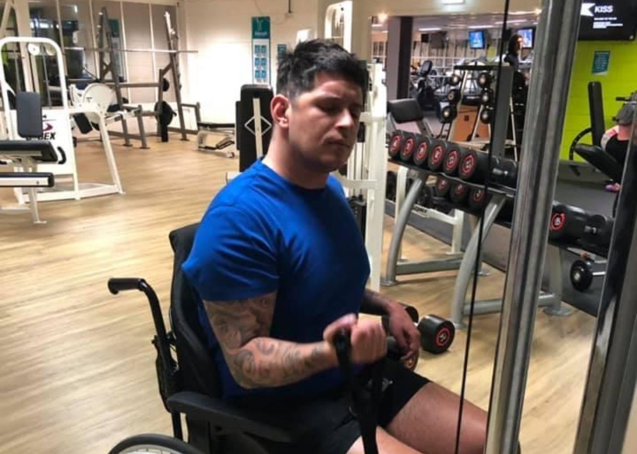 Marlon at the gym, sitting on a wheelchair, lifting weights