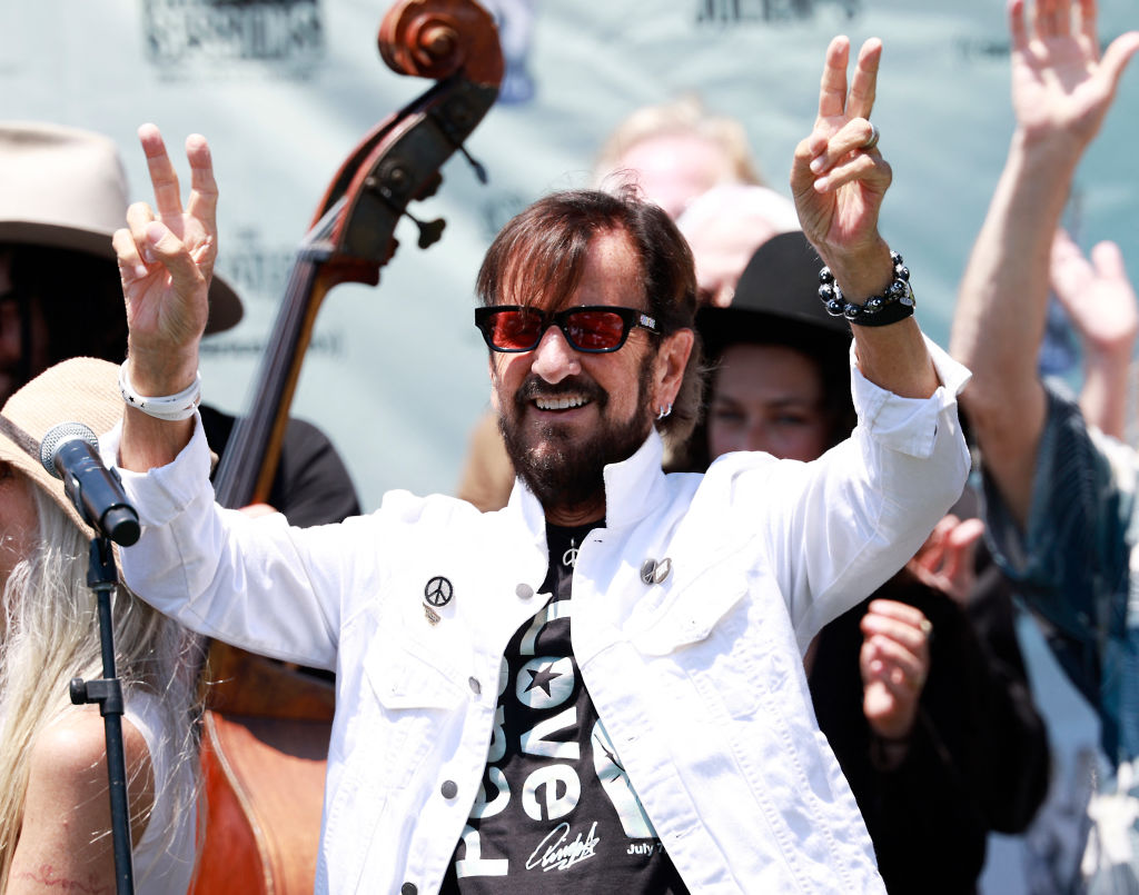 Ringo Starr smiling and holding up peace signs 
