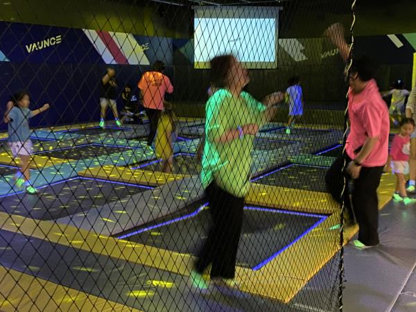 Grown-ups and children bounce on trampolines under neon laser lights. (Hwang Joo-young/The Korea Herald)