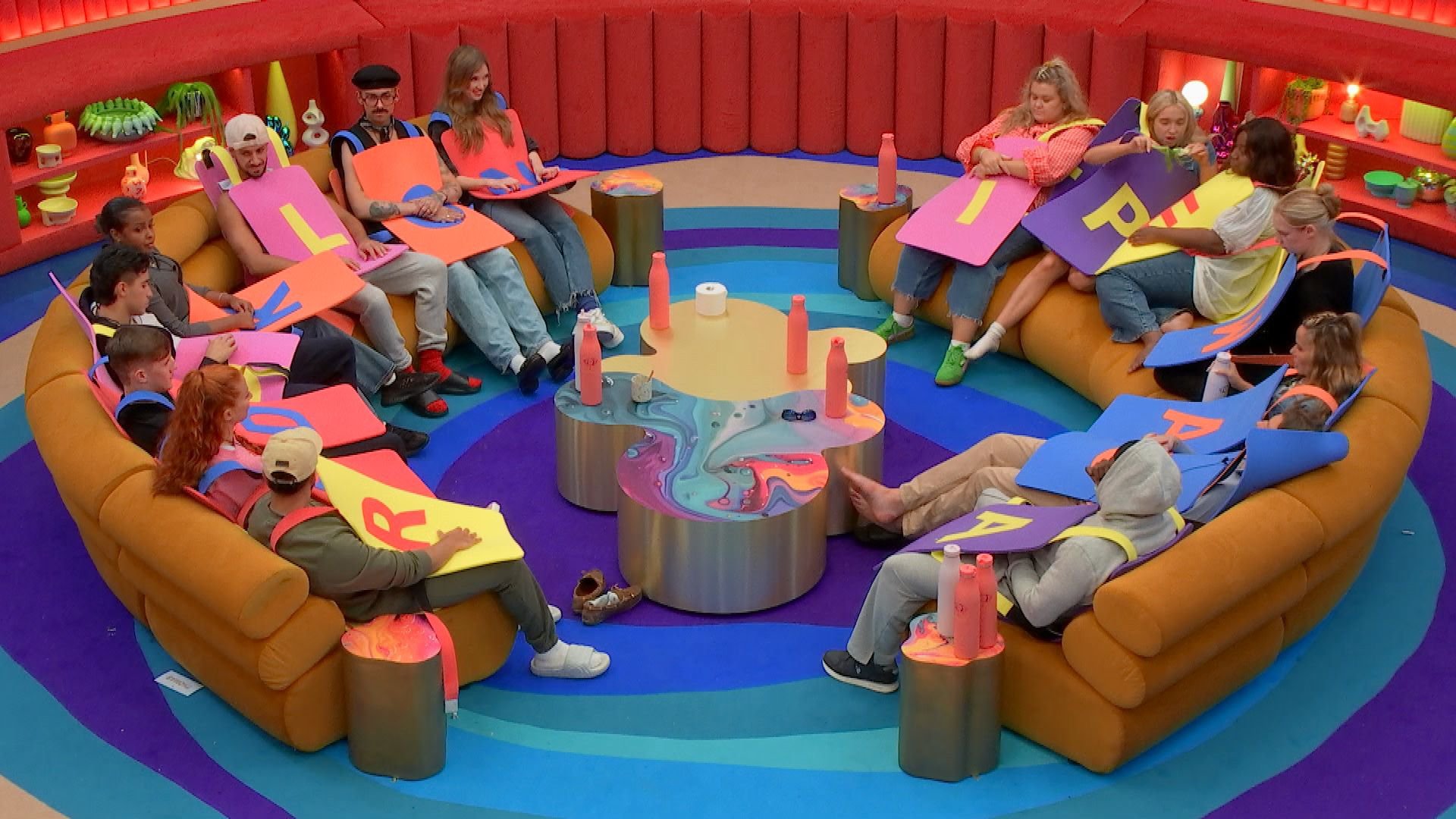 Housemates gathered in the lounge, all dressed as letters in Big Brother