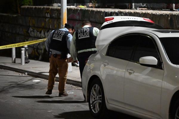 Two police officers look at the ground behind a white Infiniti SUV as they search for clues at the site of a mass shooting in Greenpoint.