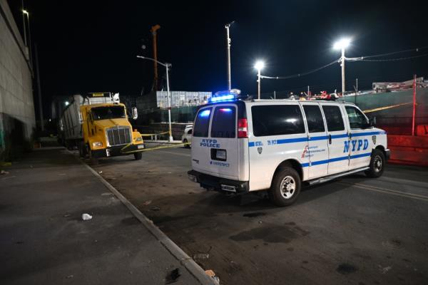 A police van is parked alongside yellow tape cordoning off the shooting site in Brooklyn, where a tractor trailer is parked in the background.