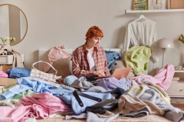 Indoor shot of short haired ginger woman surrounded by clothes from wardrobe sells different items of clothing online via laptop computer sits in bed against bedroom interior. Sor...(3004 chars omitted)...g elegance pink sandals into suitcase ready to summer travel vacation sitting on bed. Tourist female packing baggage with clothes, accessories, shoes preparation to tourism