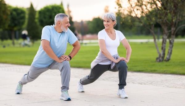 Active happy elderly couple in sportswear working out together in city park in morning