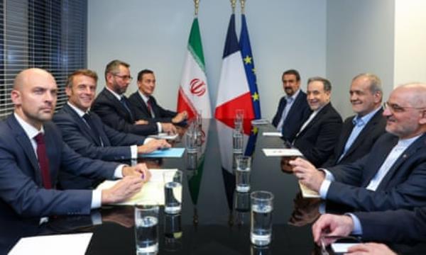 Macron with an entourage sits directly opposite Pezeshkian with his entourage at a table