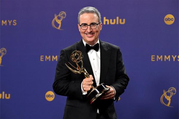 John Oliver in a suit holding a trophy
