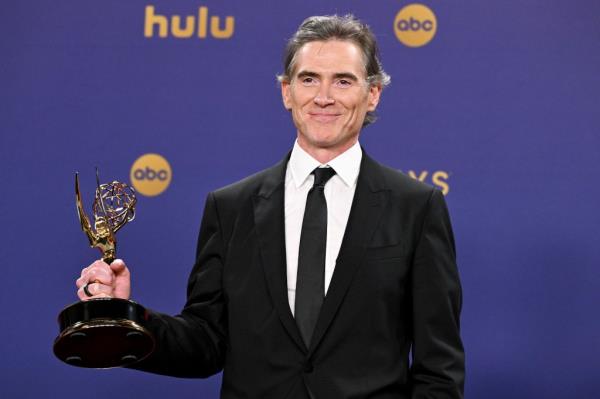 Billy Crudup in a suit holding a trophy
