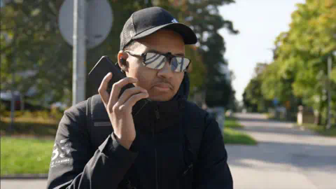 BBC Picture of Charles-Emmanuel Mikko Rasanen, wearing a black coat, sunshades and a black cap, holding a mobile phone on a road near his house in Finland