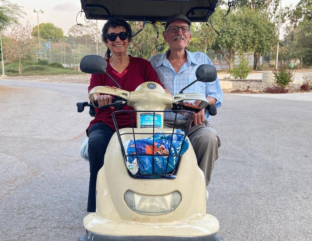 Sharone's parents in a mobility cart together, in the middle of the street, smiling