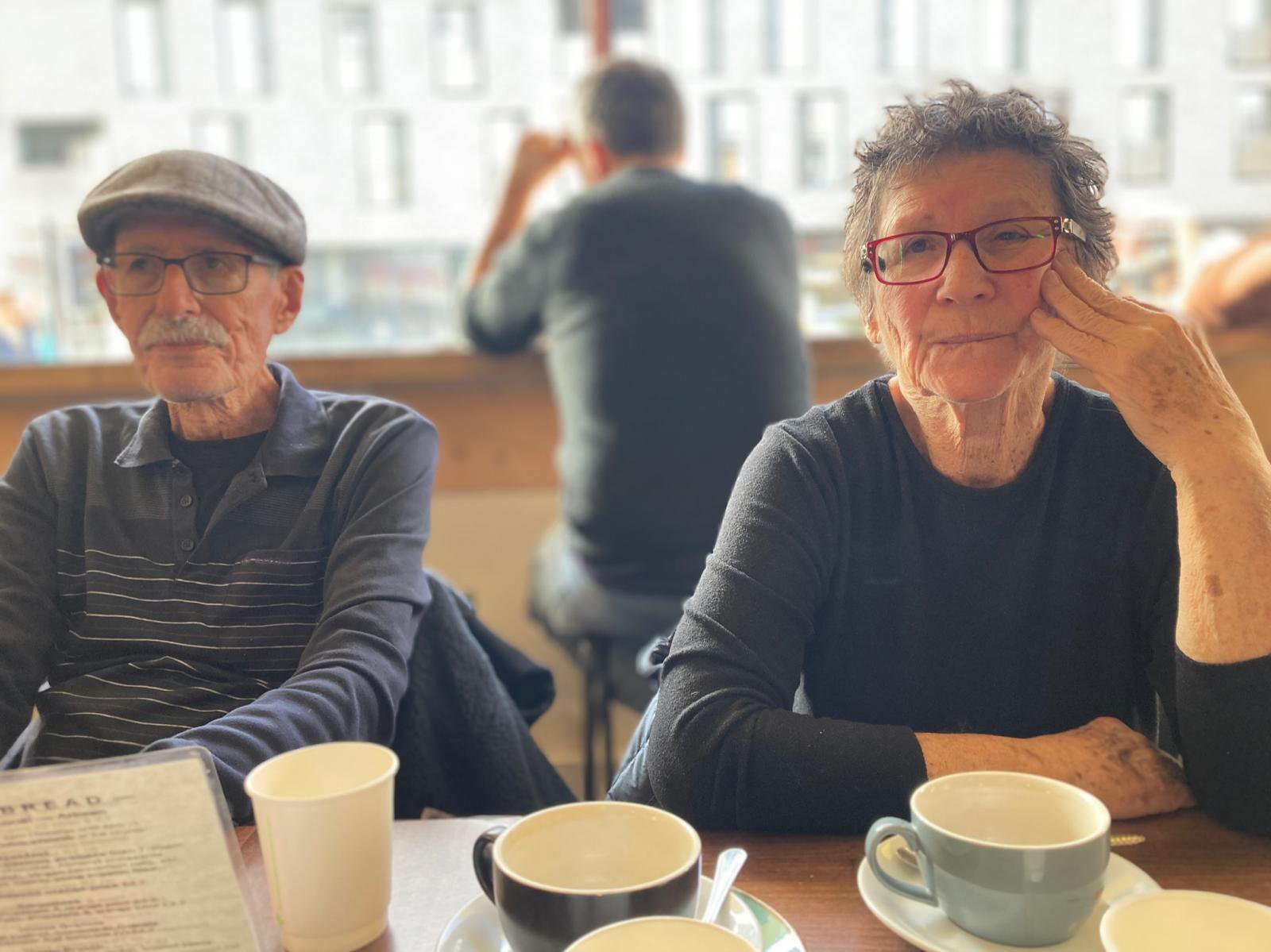 Sharone's parents sitting in a cafe, with coffee's on the table